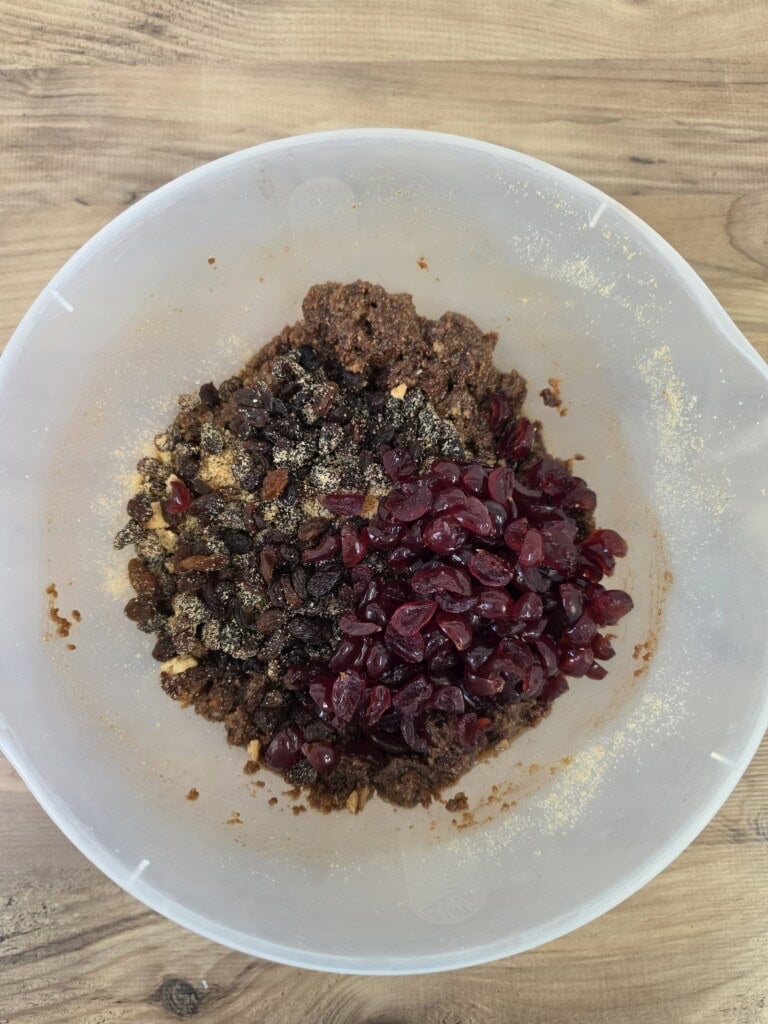 A translucent bowl containing a mixture of dark chocolate tiffin mixture, raisins, and dried cranberries.