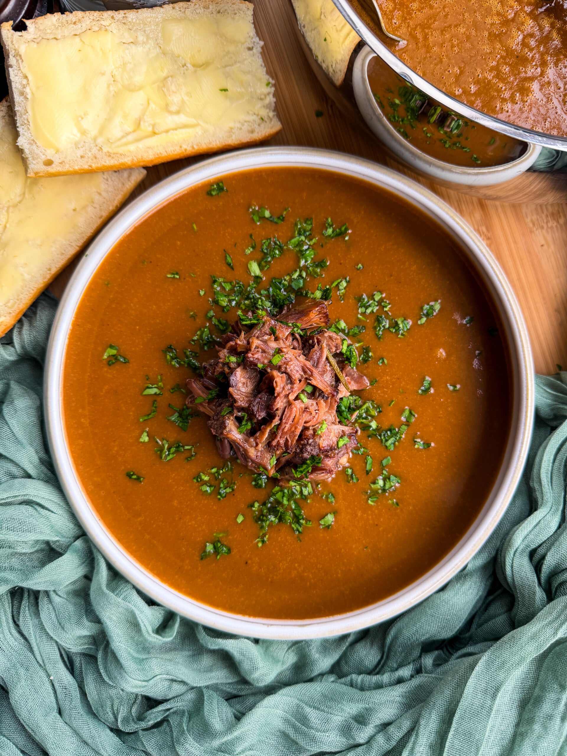 A bowl of oxtail soup topped with shredded oxtail and herbs, served with two slices of buttered bread.