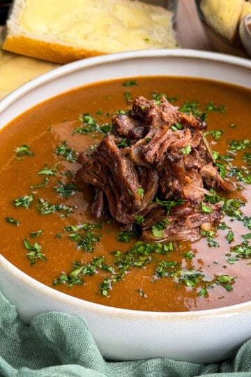 A bowl of oxtail soup topped with shredded beef and herbs, served with slices of buttered bread.