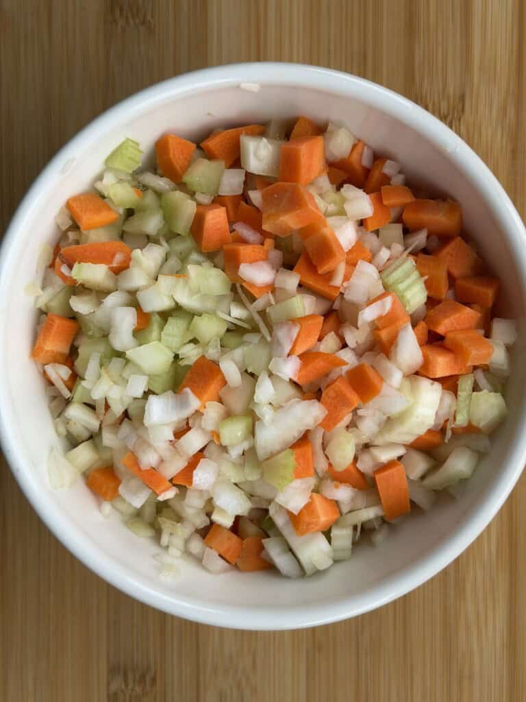 A white bowl filled with a chopped mixture of carrots, celery, and onions.
