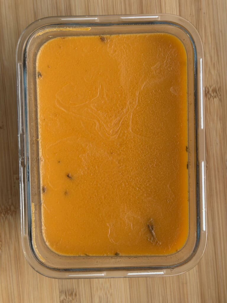 A glass rectangular container filled with orange soup on a wooden surface.