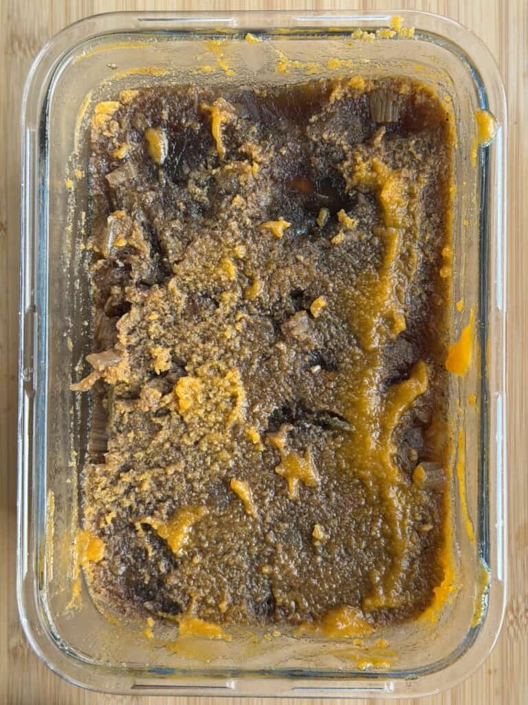 A rectangular glass container filled with a thick, dark brown stew featuring visible pieces of orange vegetable.