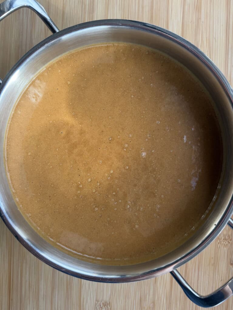 A stainless steel saucepan filled with a smooth, orange-coloured soup.