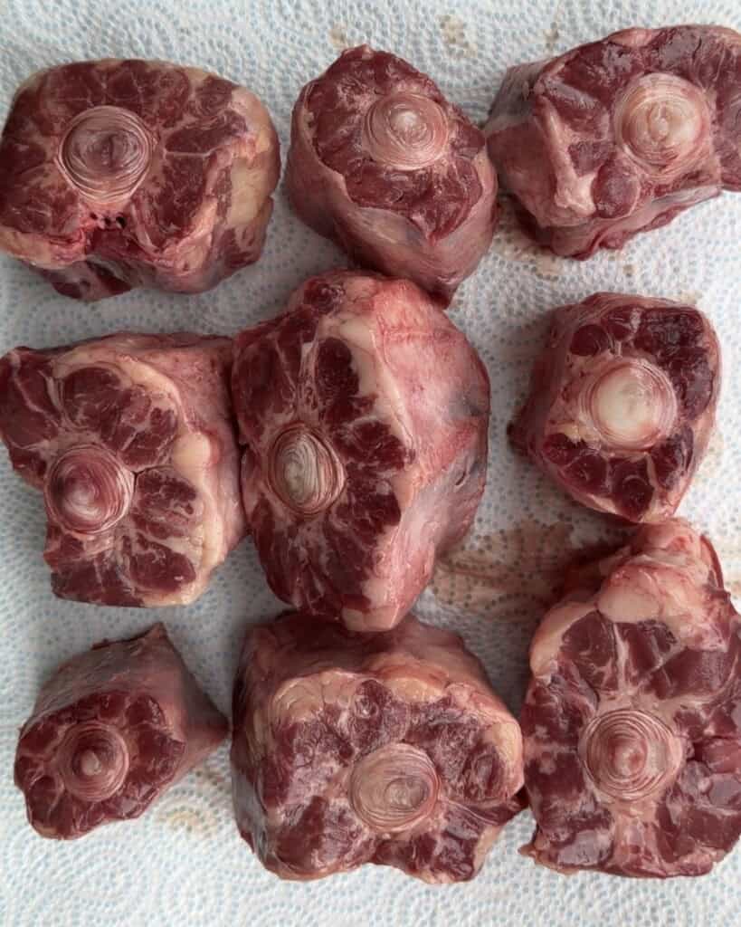 Eight raw, bone-in oxtail pieces arranged on a paper towel.