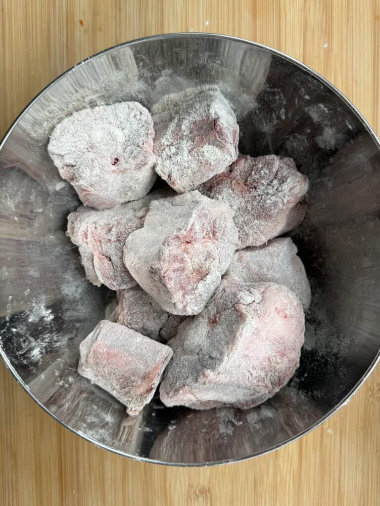 Raw oxtail pieces coated in flour inside a metal bowl.