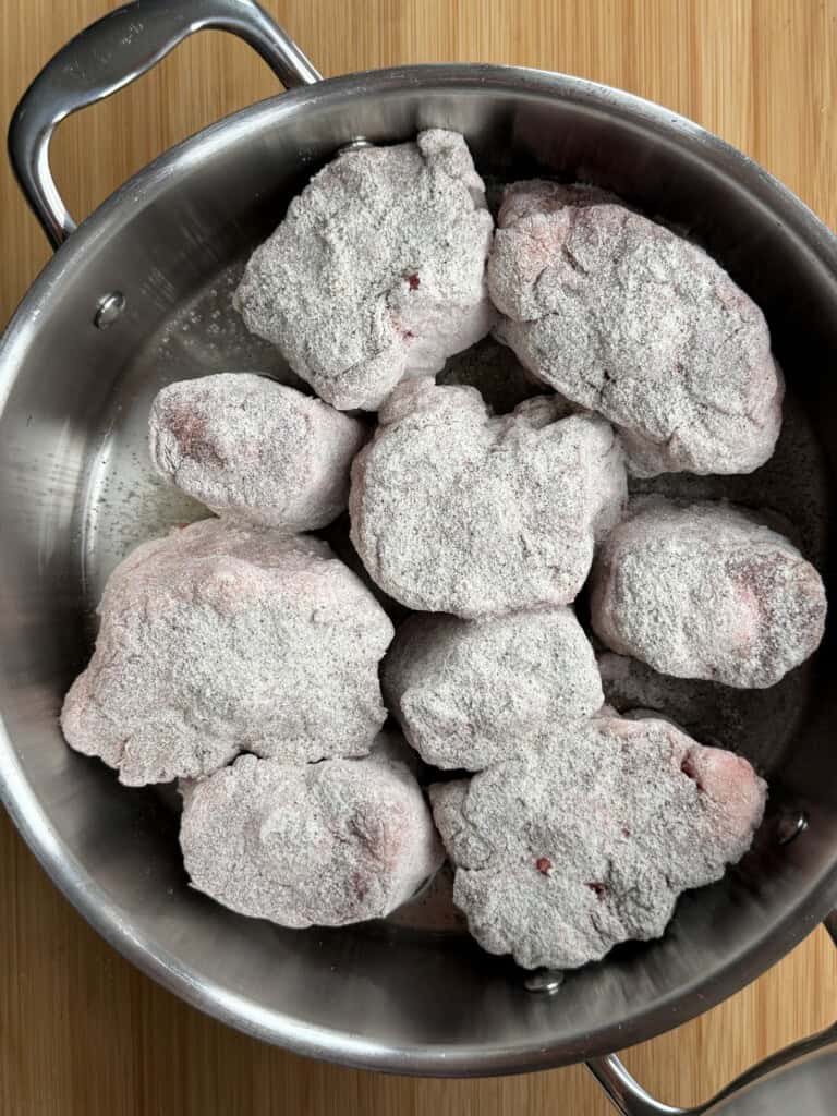 Flour-coated pieces of raw meat in a stainless steel saucepan.