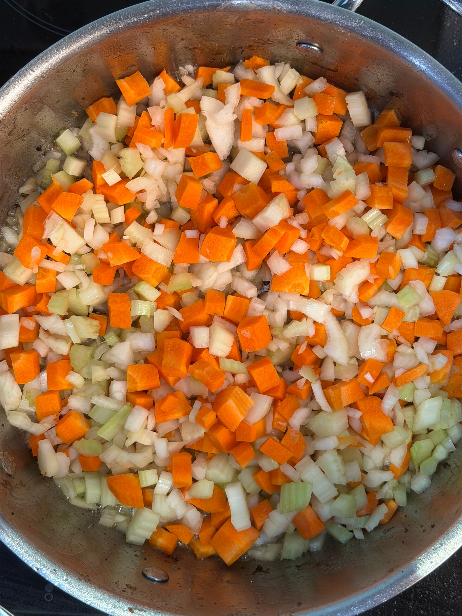 Diced carrots, onions, and celery sautéing in a stainless steel frying pan.