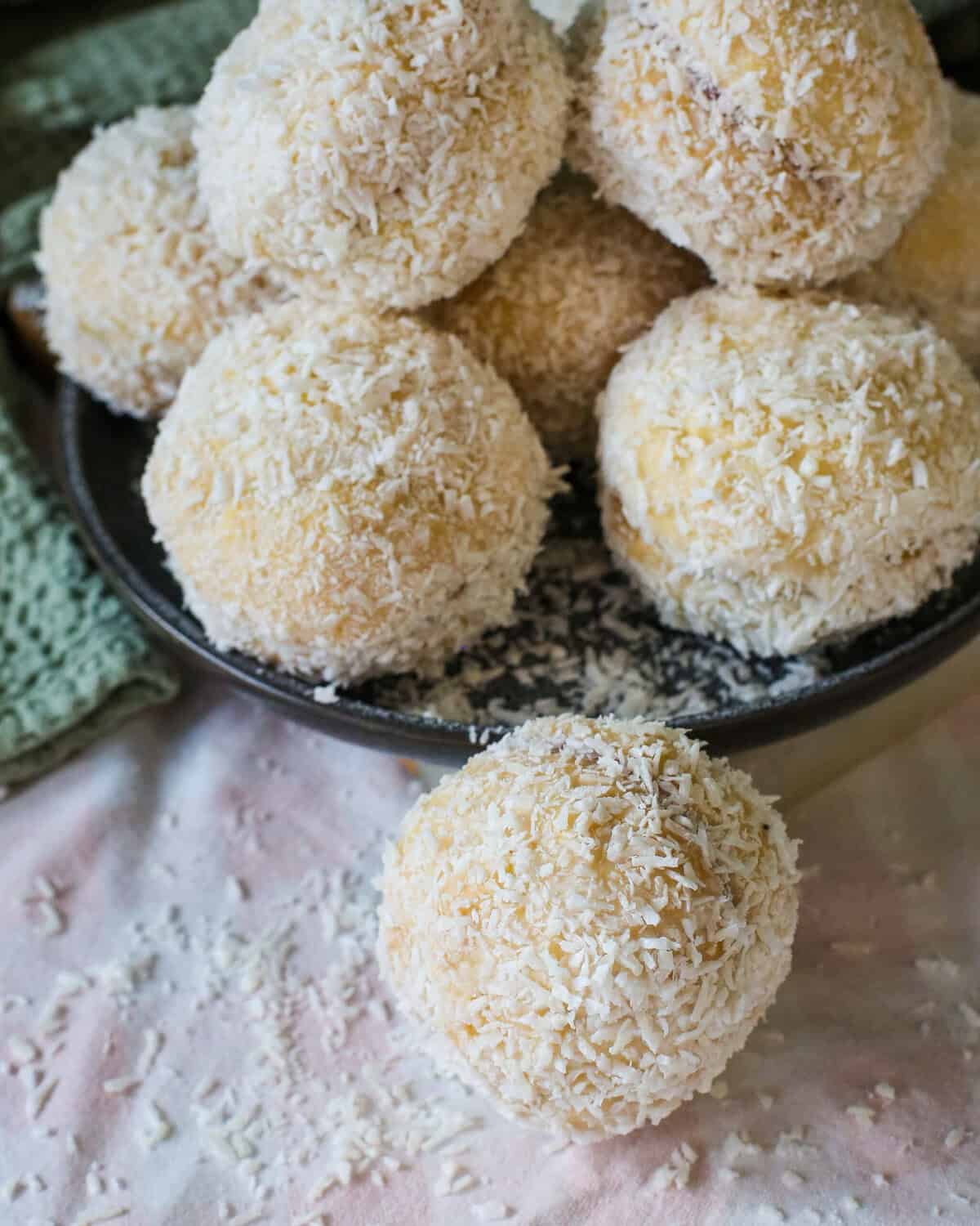 A pile of round, coconut-covered Scottish snowballs on a plate with one biscuit in the foreground.