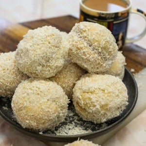 A plate piled with coconut-covered Scottish snowballs next to a mug of coffee.