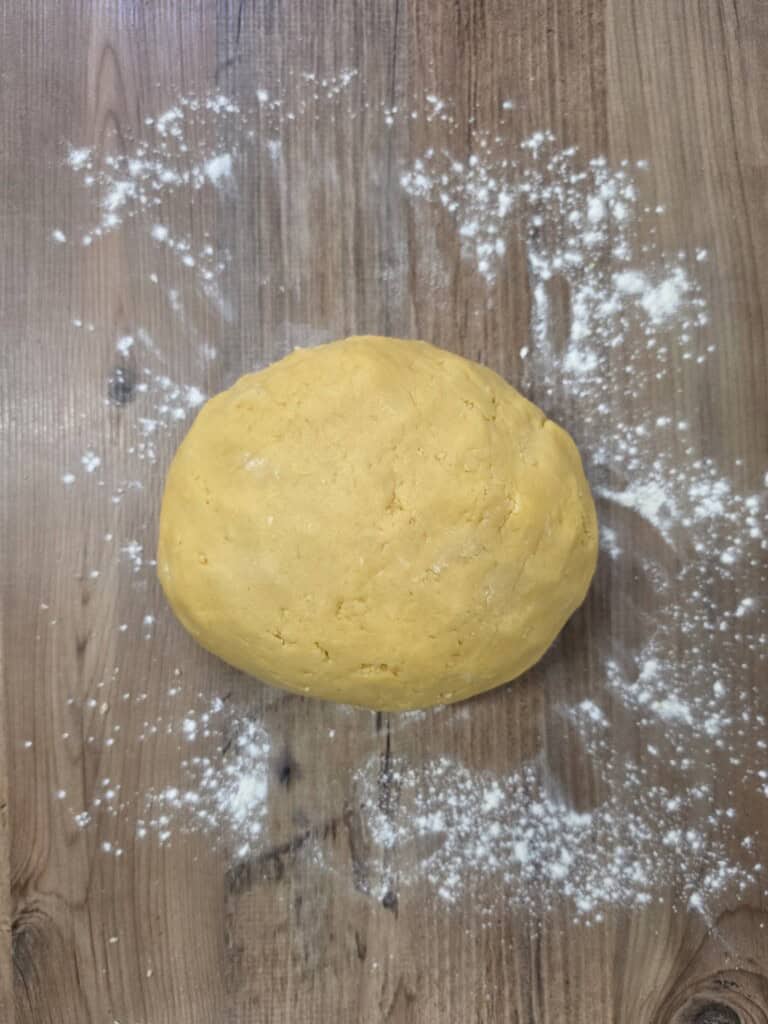A ball of yellow dough sits on a wooden surface dusted with flour.