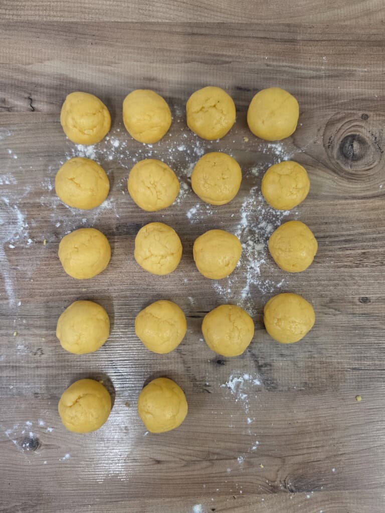 Eighteen yellow dough balls arranged in a grid on a floured wooden surface.