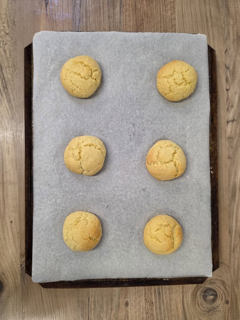 Six round, pale-yellow biscuits arranged in two columns on a parchment-lined baking tray.