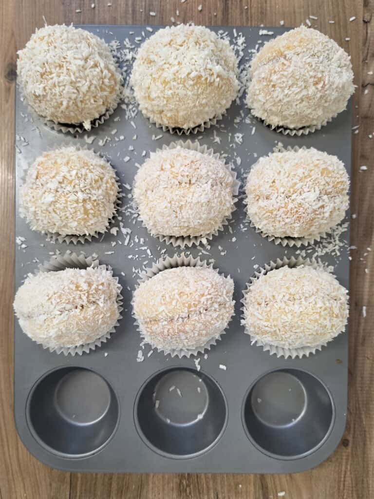 Nine fairy cakes topped with white coconut shavings in a bun tin.