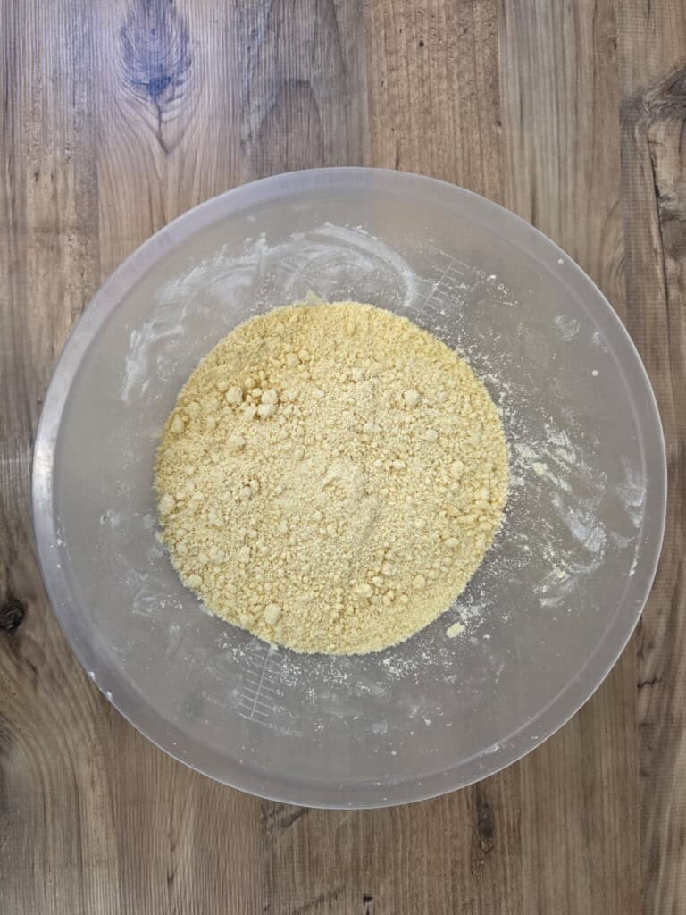 A large mixing bowl containing a crumbly, yellow flour and butter mixture.