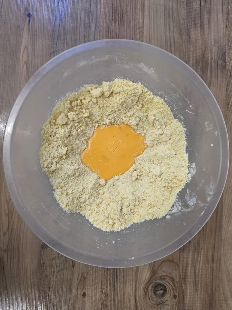 A raw egg yolk in the centre of a bowl of flour-based crumble mixture.
