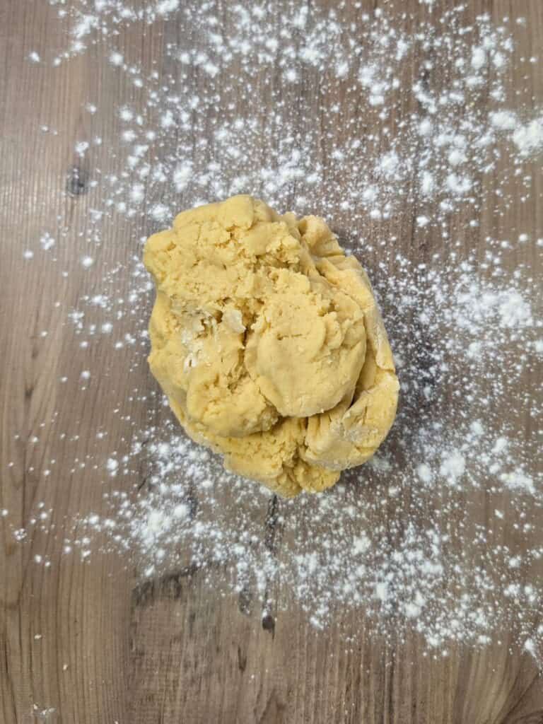 A ball of yellow dough centred on a wooden surface dusted with flour.